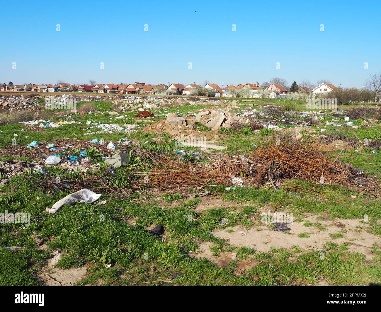 garbage dump near the village. Chaotic unofficial dump. Plastic, bags, paper, glass, biological waste. Green grass next to dirt. Ecological catastrophy. Stock Photo