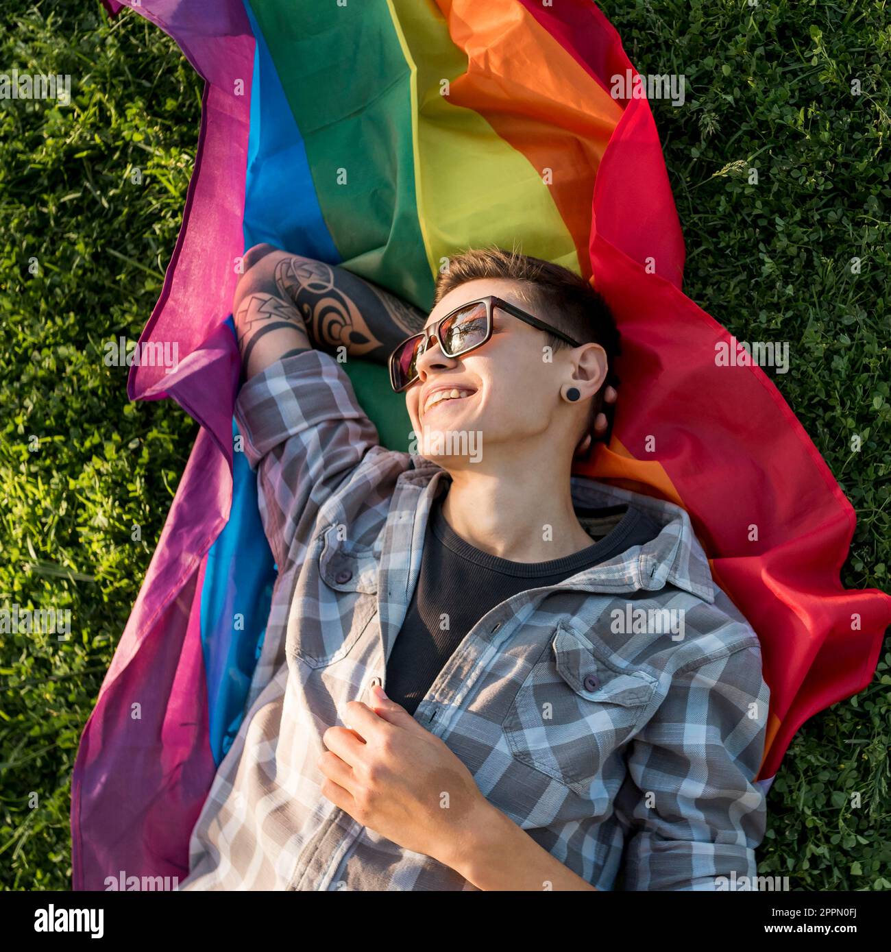 Cheerful young person lying lgbt flag park Stock Photo