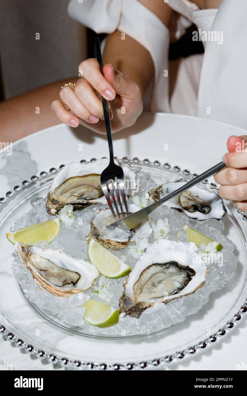 Hands of a young girl with utensils closeup eating oysters in a