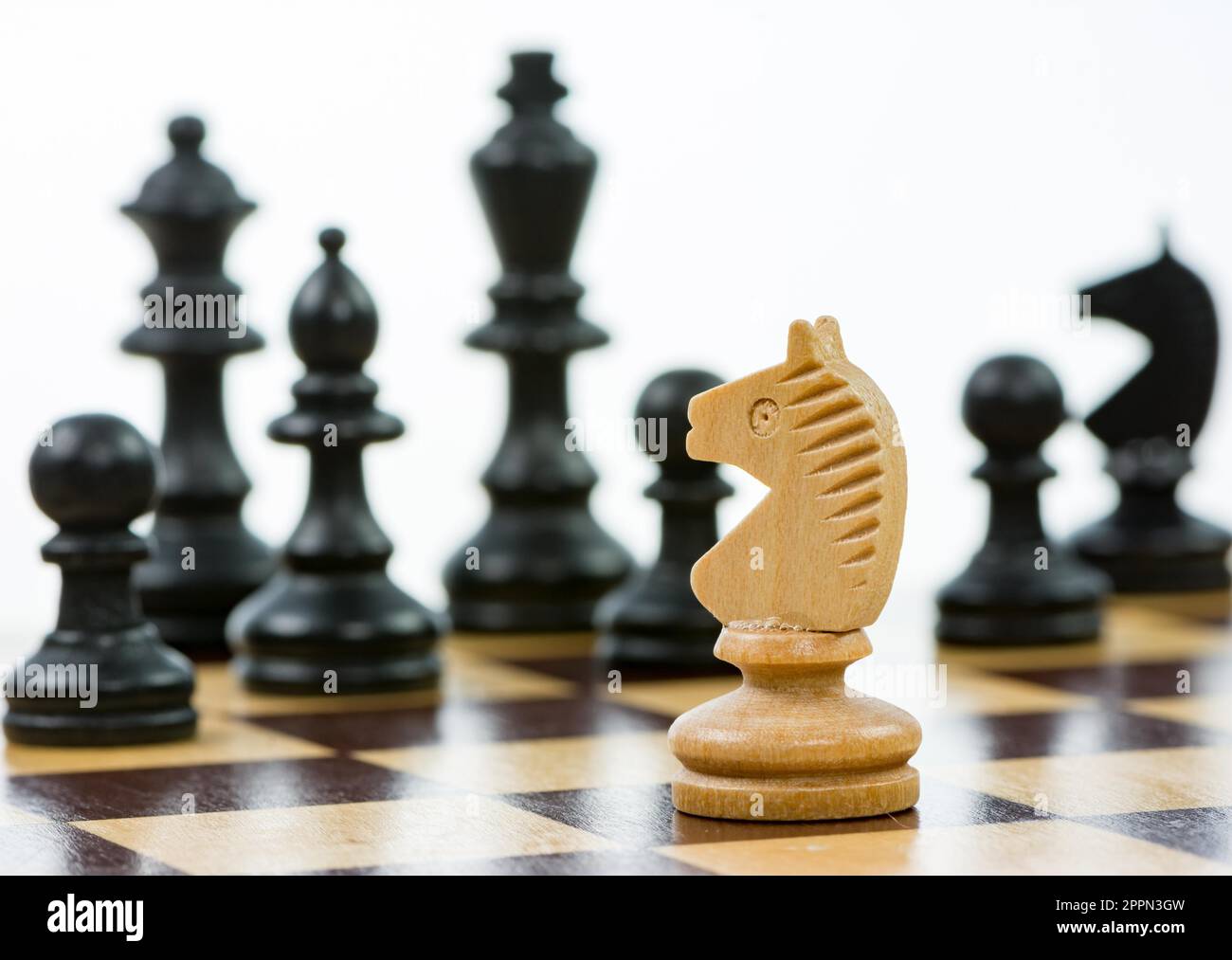 White knight against a superiority of black chess pieces on a chess board. Selective focus Stock Photo