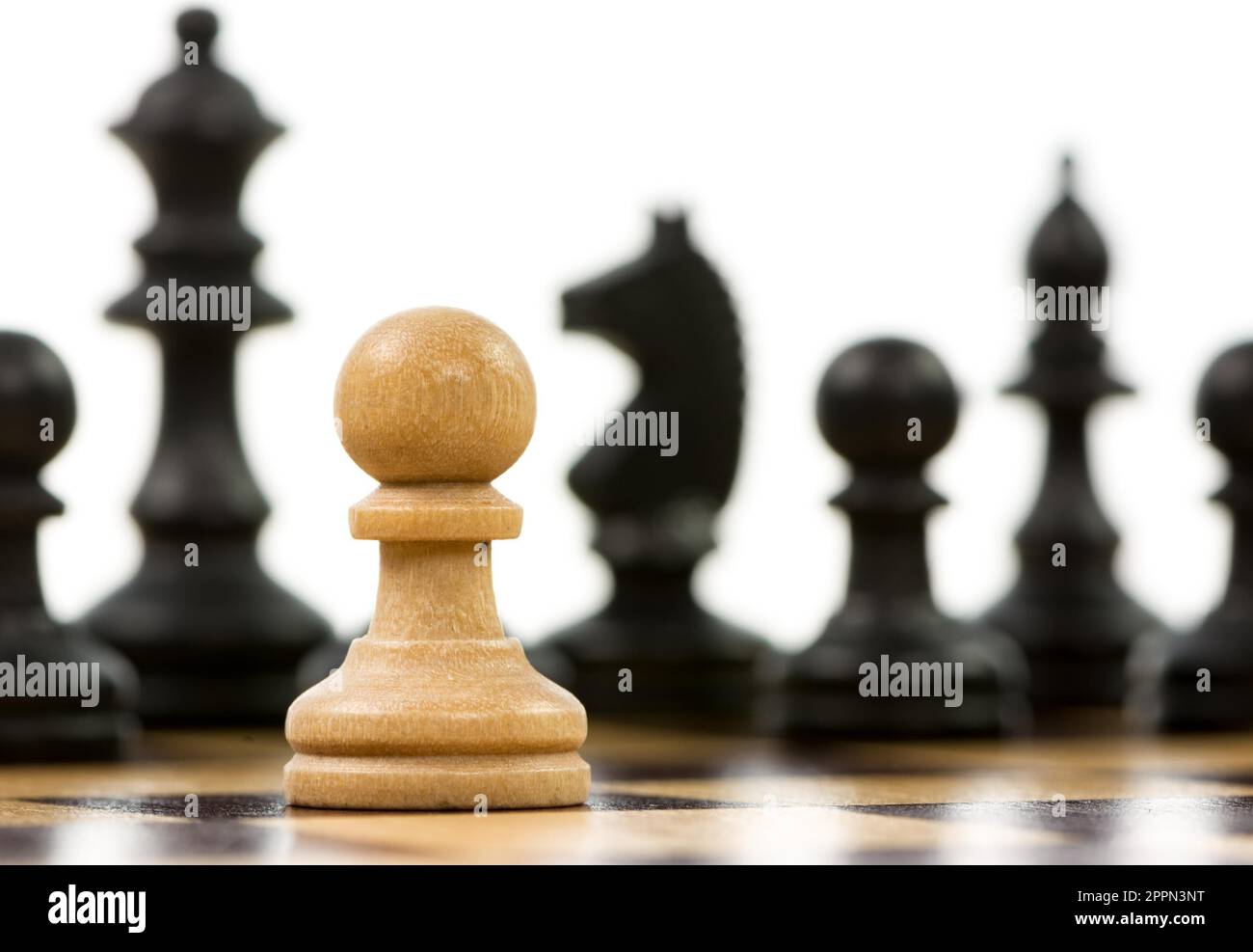 White pawn against a superiority of black chess pieces on a chess board. Selective focus Stock Photo