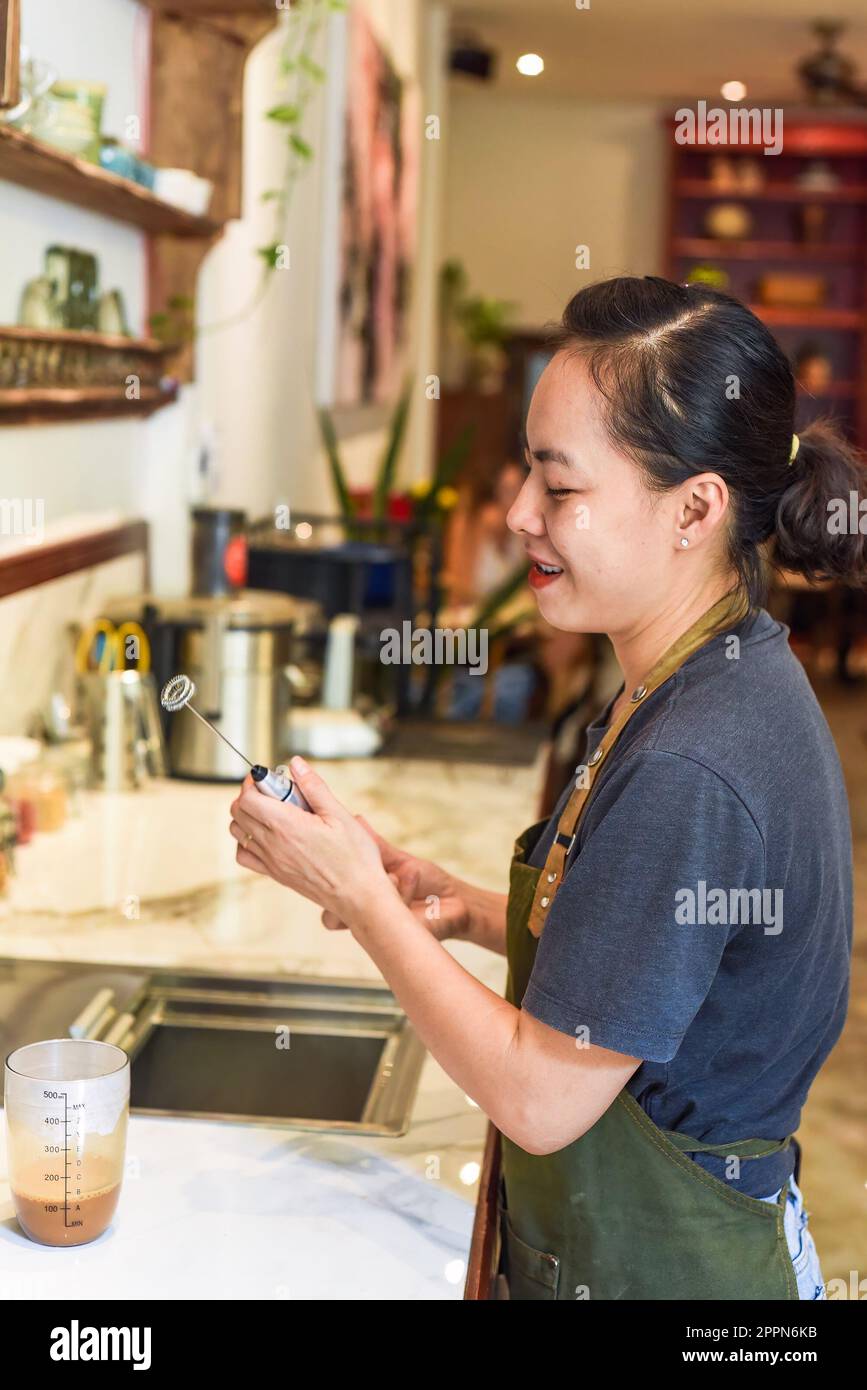 Vietnamese barista holding a mixer for condensed milk in glass cup for