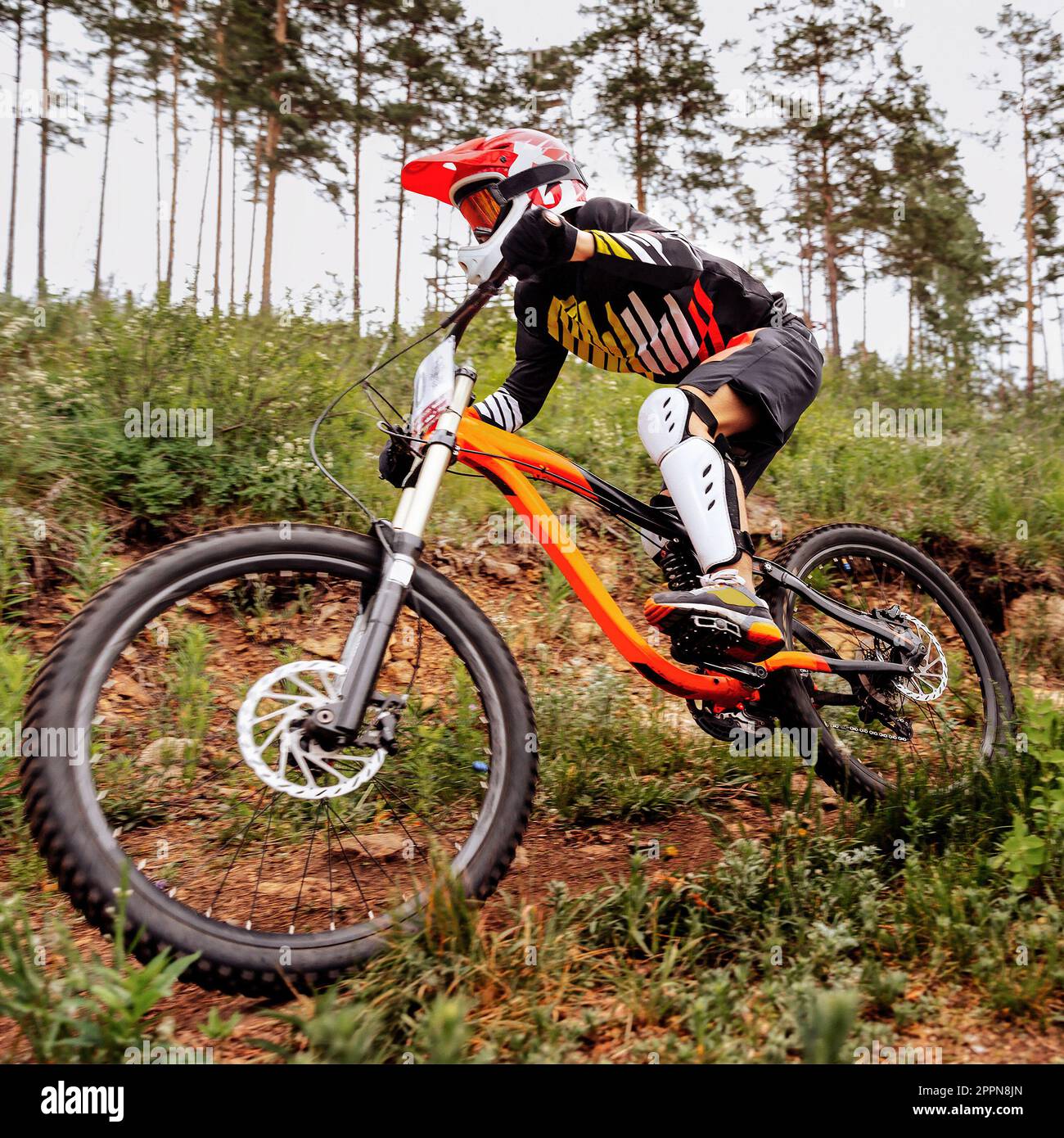 close-up racer athlete riding downhill race in mountain bike, on him protection knee and shin guard, helmet Stock Photo