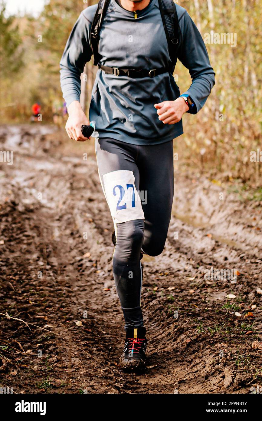 athlete runner running on iimpassability dirt road autumn marathon, sports number on leg jogger Stock Photo