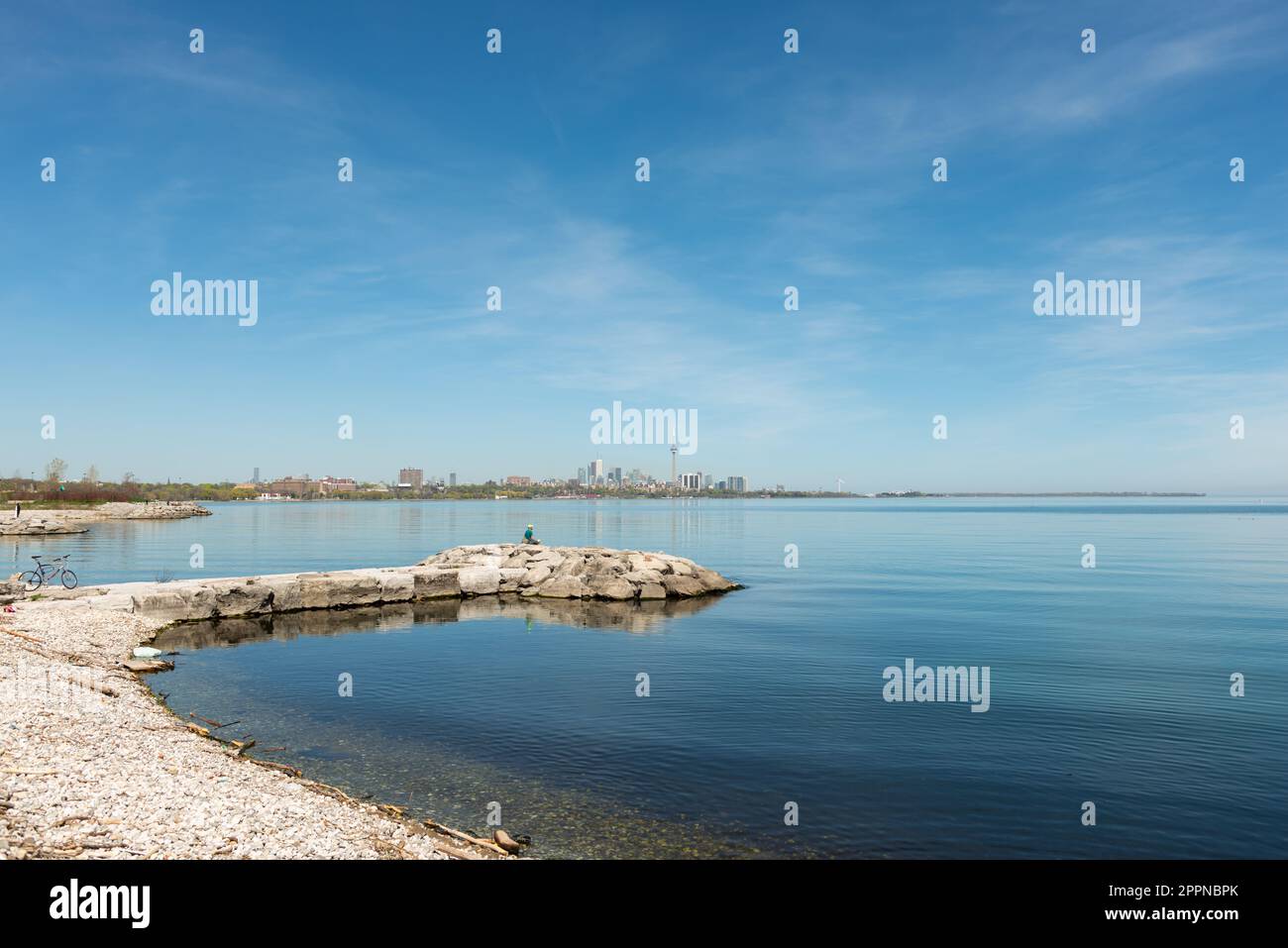 view of Lake Ontario with view of downtown skyline with figure sitting on jetty and a newly wed couple (far left) Stock Photo
