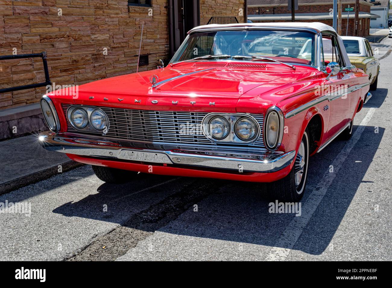 A bright red fully restored to original condition early 1960's Plymouth sport fury convertible top 2-door park alongside a building at a car show on a Stock Photo