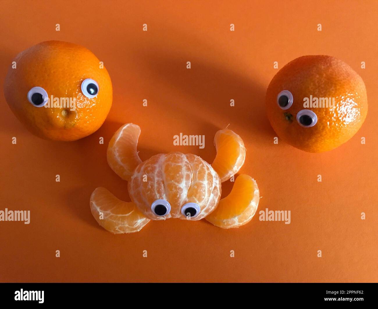 Creative funny food concept. Two googly eyed oranges looking at peeled orange segments in abstract animal shape with eyes Stock Photo