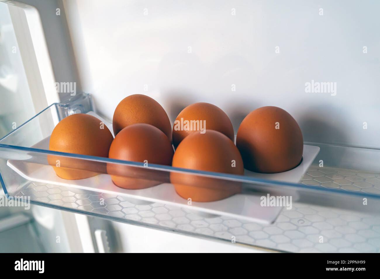 half a dozen eggs in the refrigerator tray. 6 brown chicken eggs in an