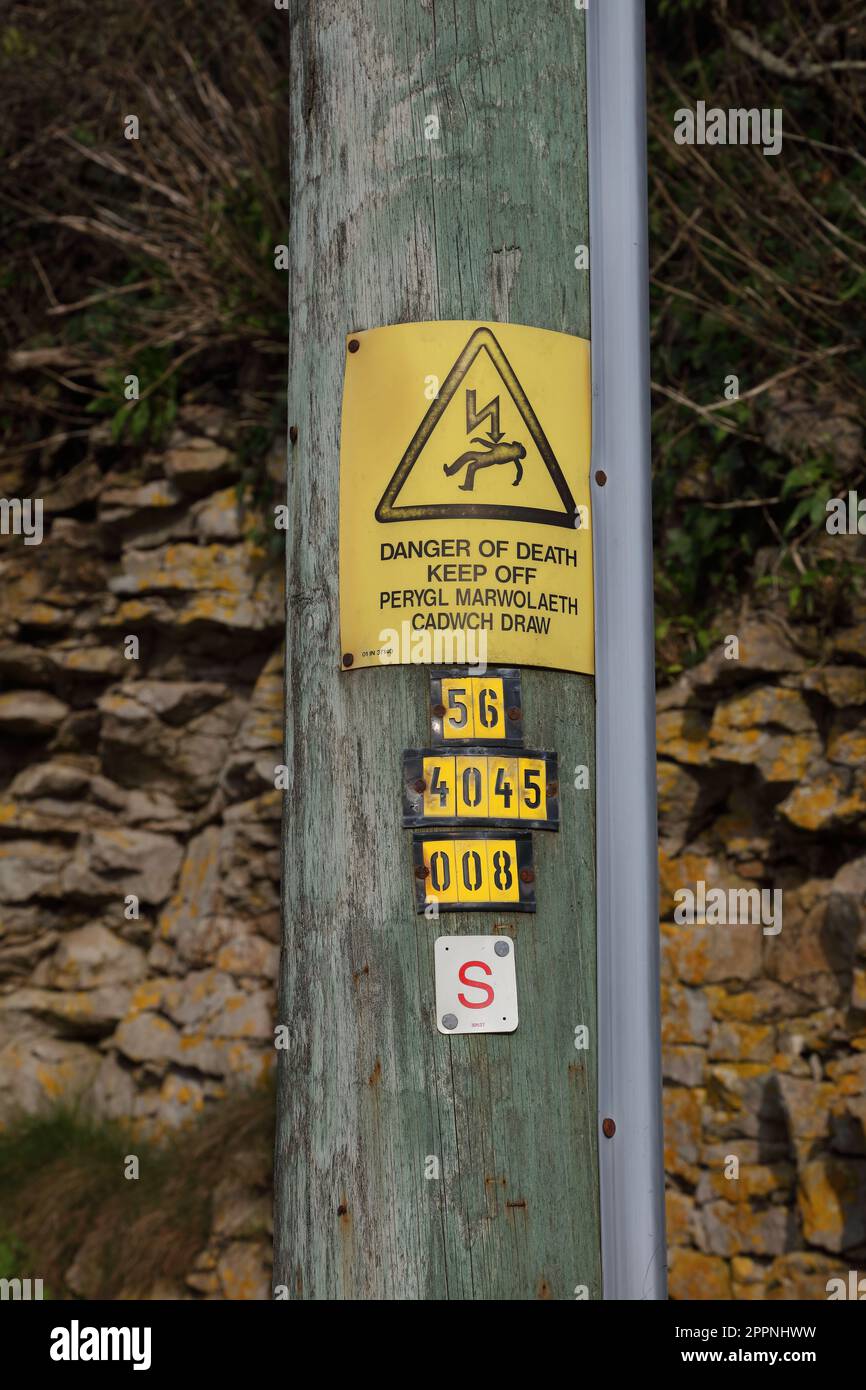 A high electricity pols standing in a rural location with a warning sign in both English and Welsh languages warning of the danger. Stock Photo