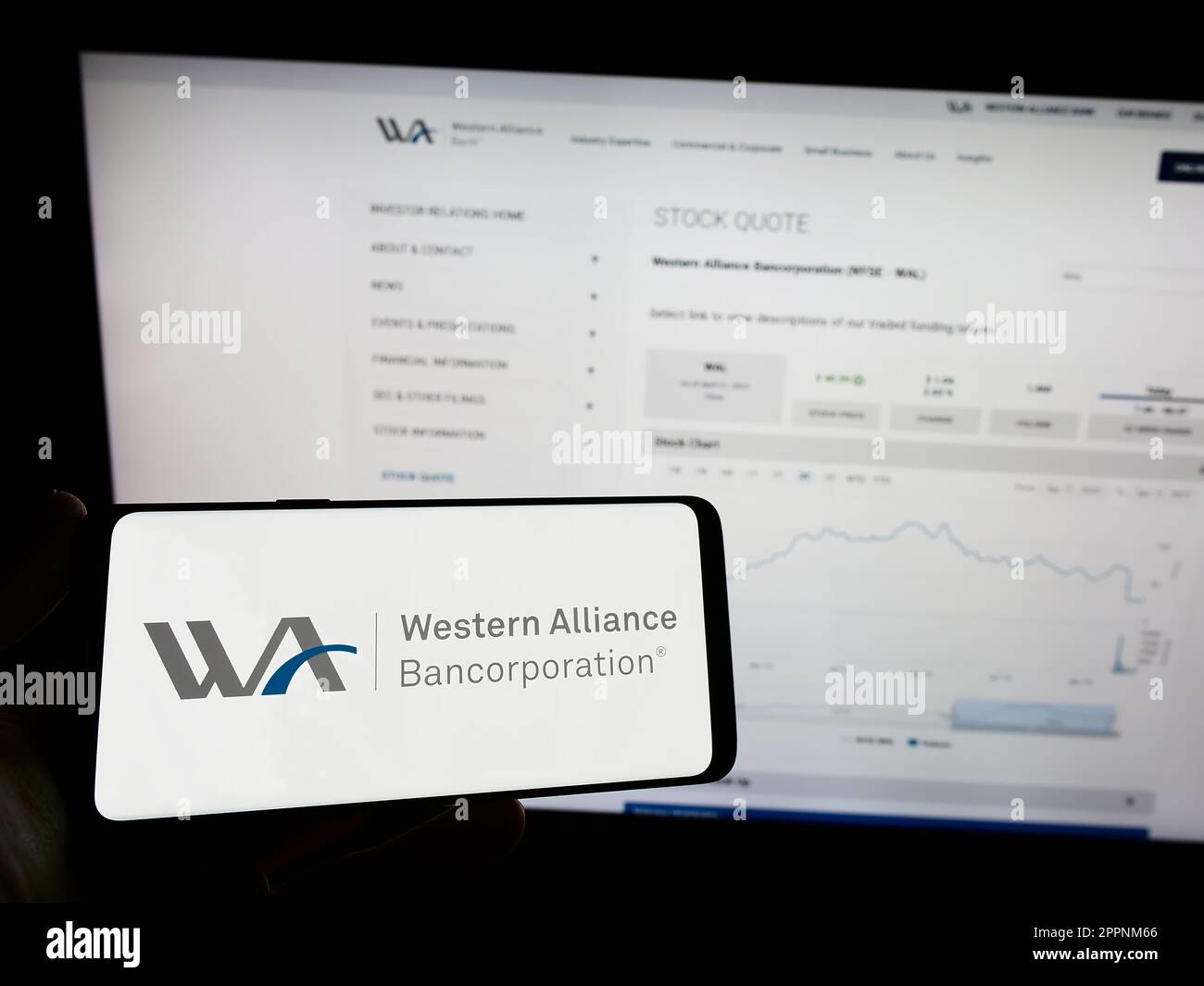 Person holding mobile phone with logo of US company Western Alliance Bancorporation on screen in front of web page. Focus on phone display. Stock Photo