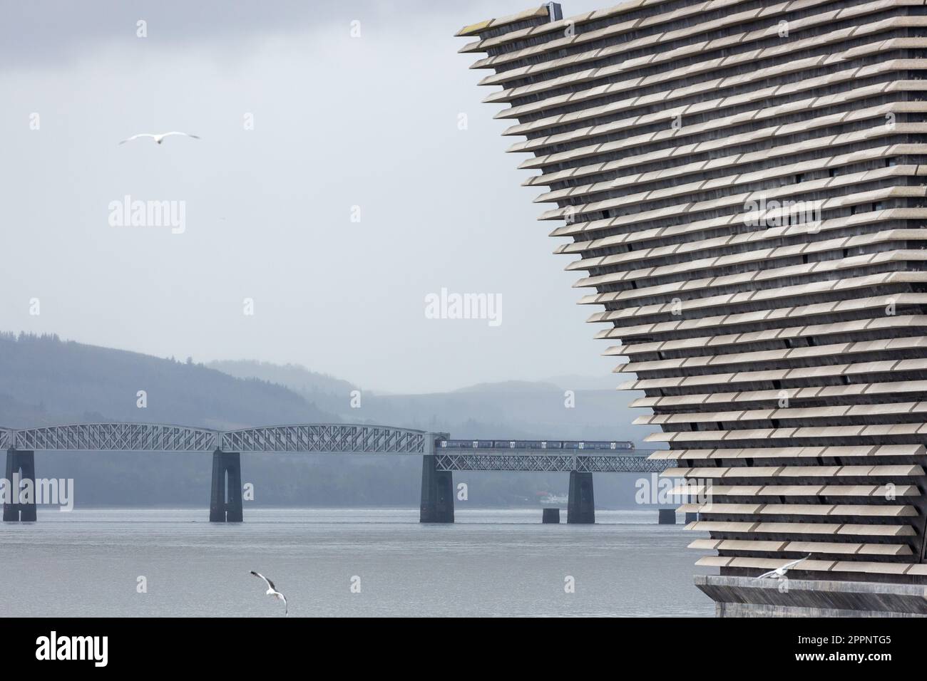 The V&A Museum with a train crossing the Tay Rail Bridge in the background, Dundee, Scotland Stock Photo