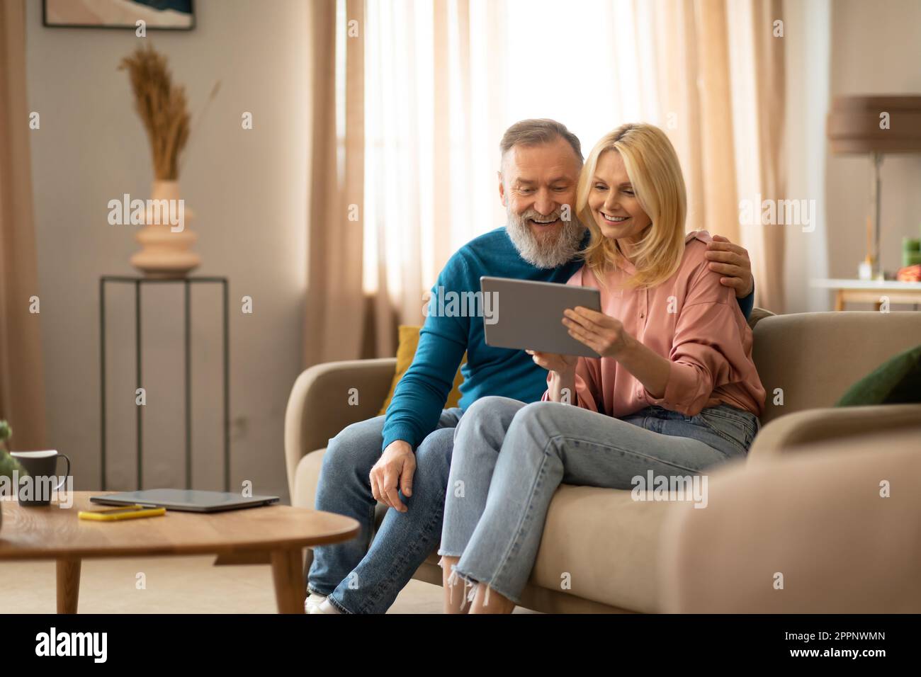 Cheerful Mature Couple Using Digital Tablet Relaxing Sitting At Home Stock Photo
