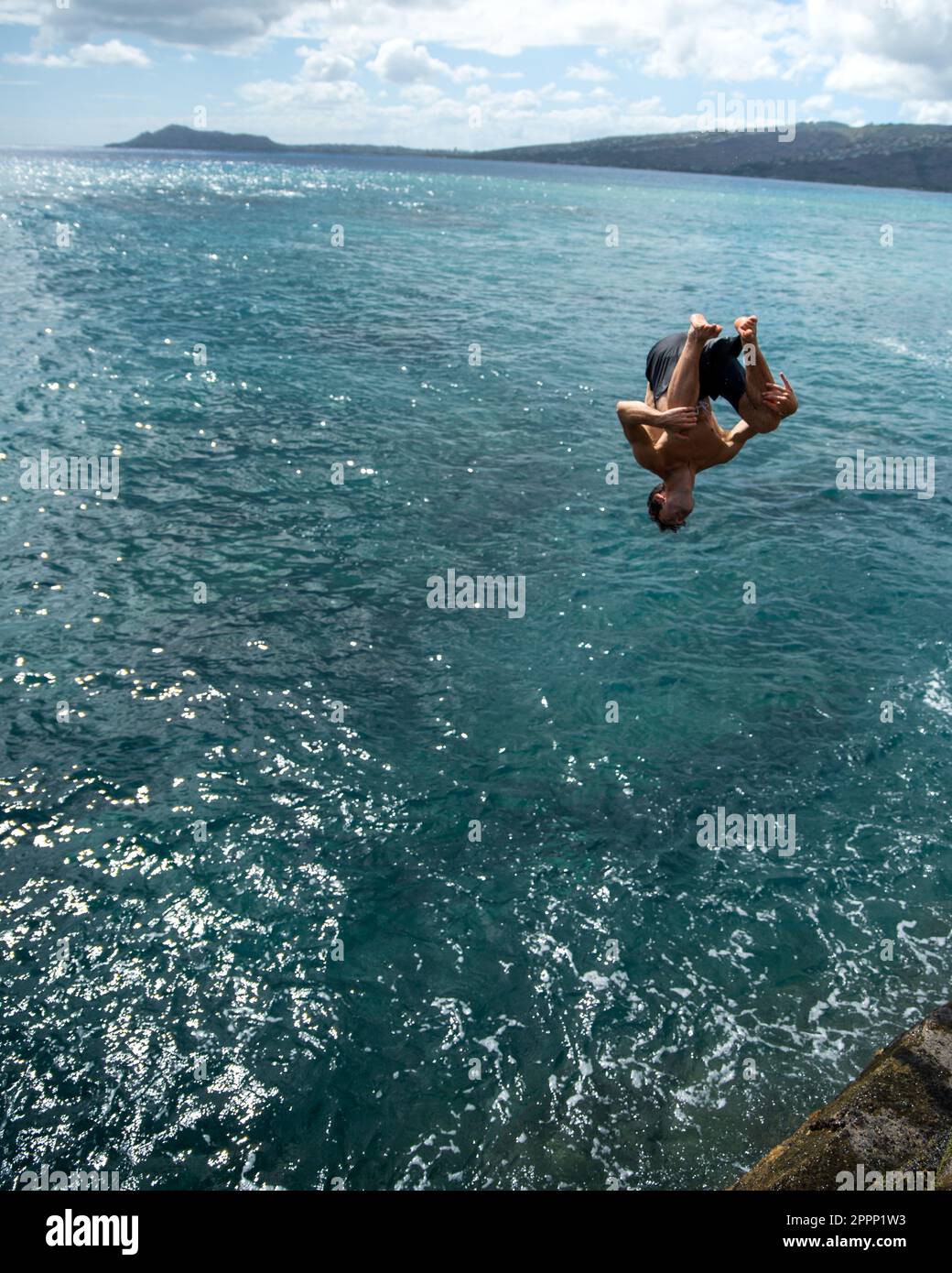 Man cliff jumping off Spitting Cave on Oahu, Hawaii. High quality photo
