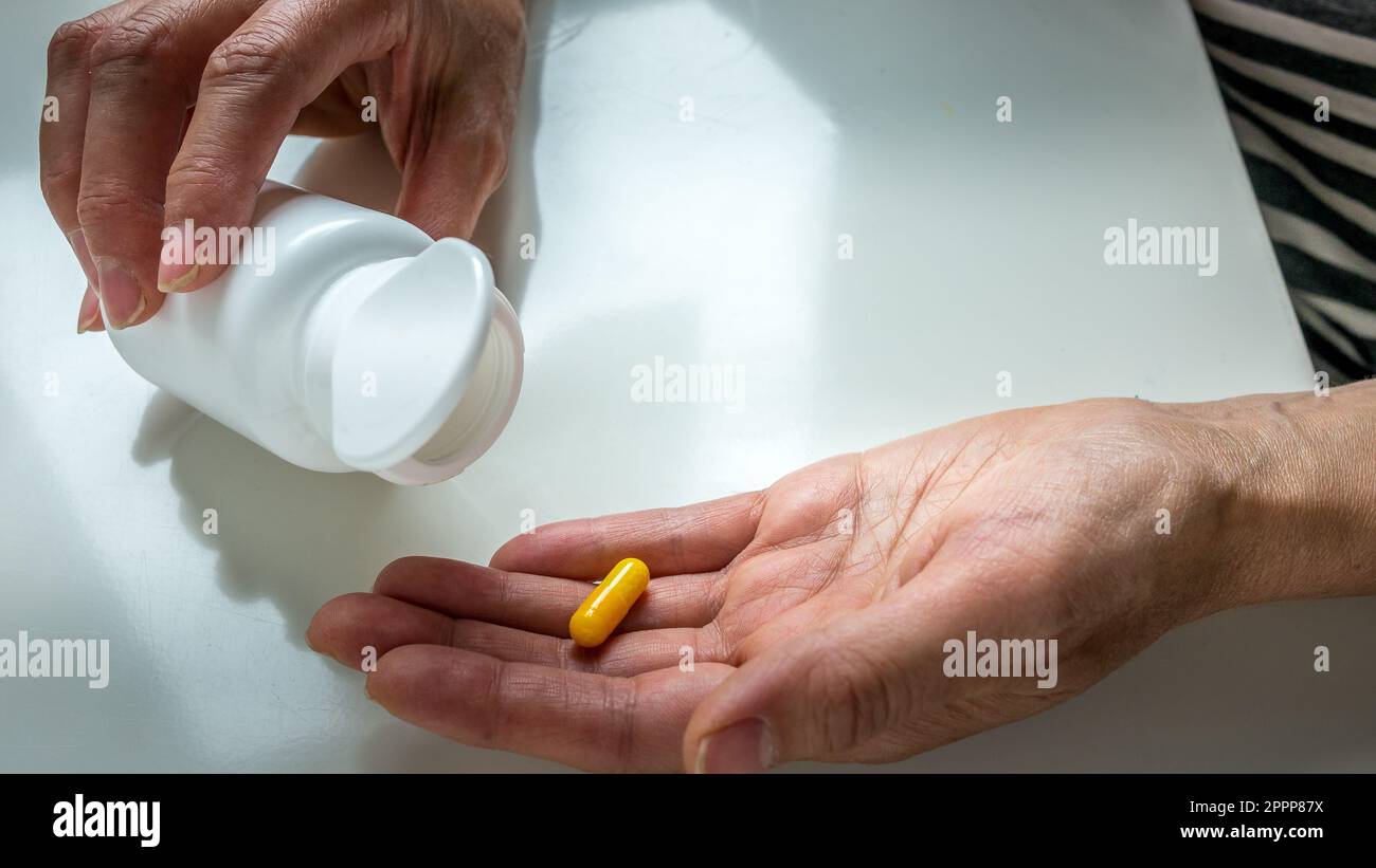 Hand with a yellow pill, coated capsule, dosing a medication from a