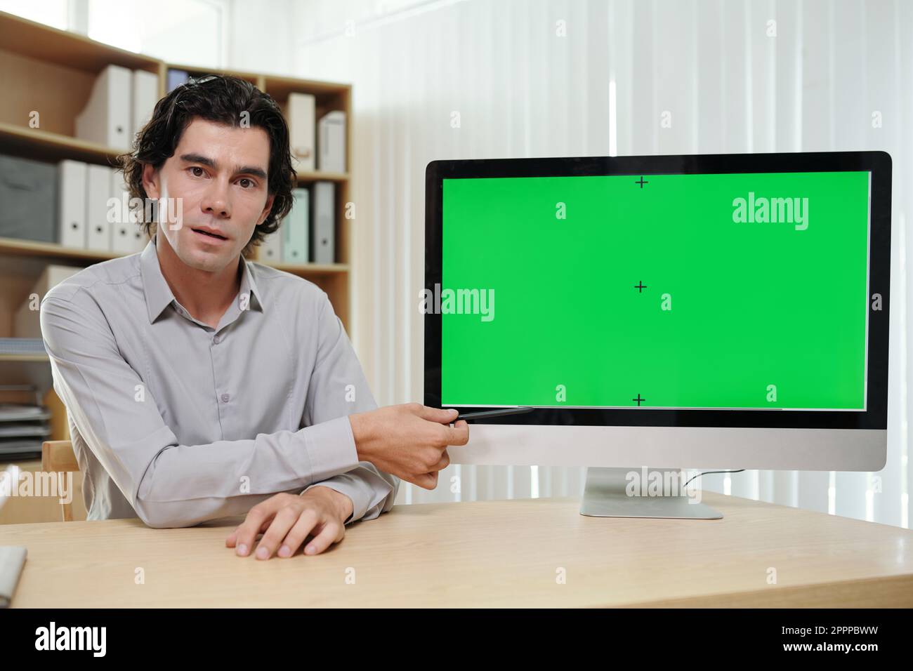 Confident businessman or coach pointing at green screen of computer while making presentation to online audience at webinar Stock Photo