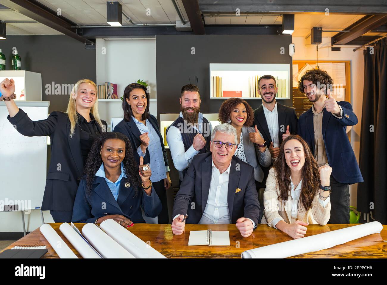 Multi-ethnic and mixed age group of entrepreneurs rejoicing at a success of their company. Sitting at the meeting table they smile in victory with the Stock Photo