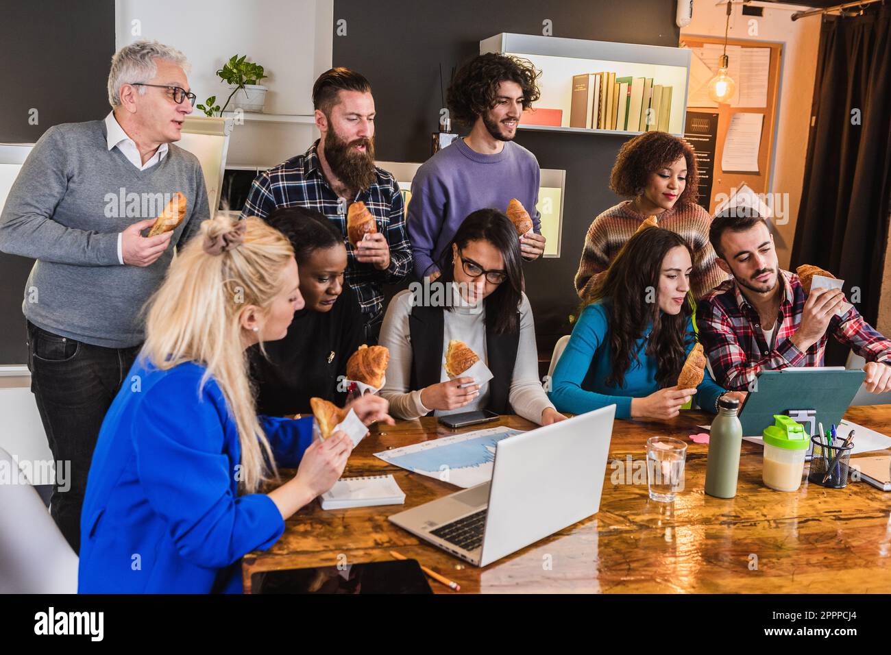 Workgroup having a discussion during a leisure break over eating croissants. Workplace snack to improve efficiency Stock Photo