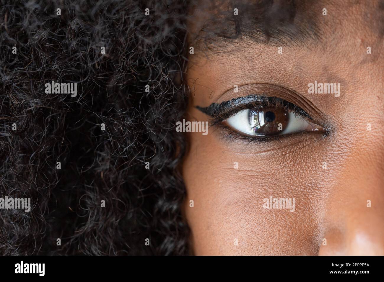 Macro of the human eye of an African woman wearing makeup with an afro hairstyle. Large black copy space on the hair and eye details with eyelashes an Stock Photo