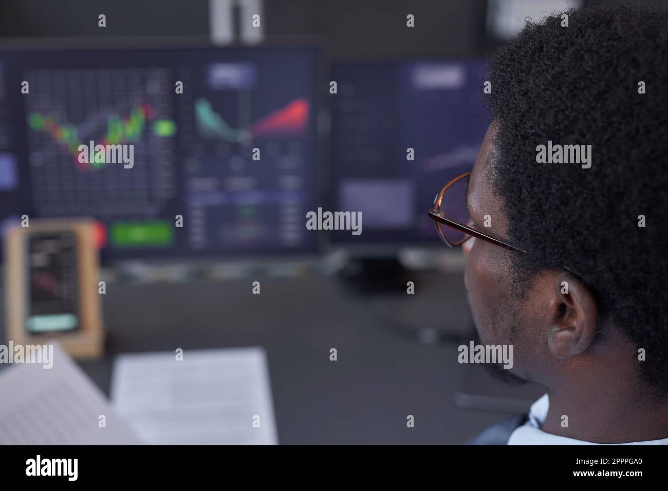 Close-up of young trader analyzing financial graphics on computers sitting at his workplace Stock Photo