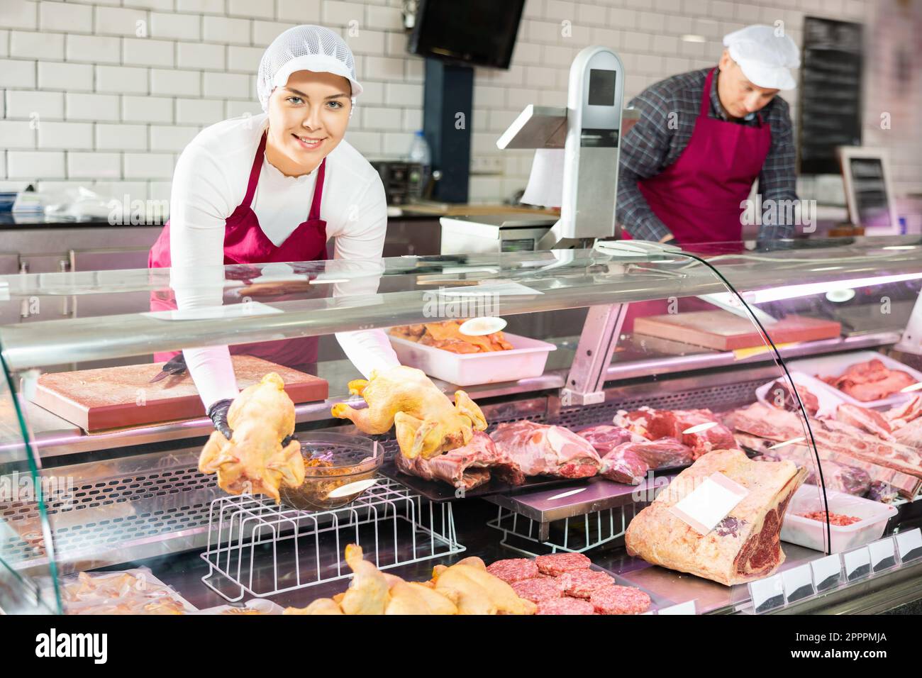 Young female butcher showing fresh whole chicken in butchery Stock Photo