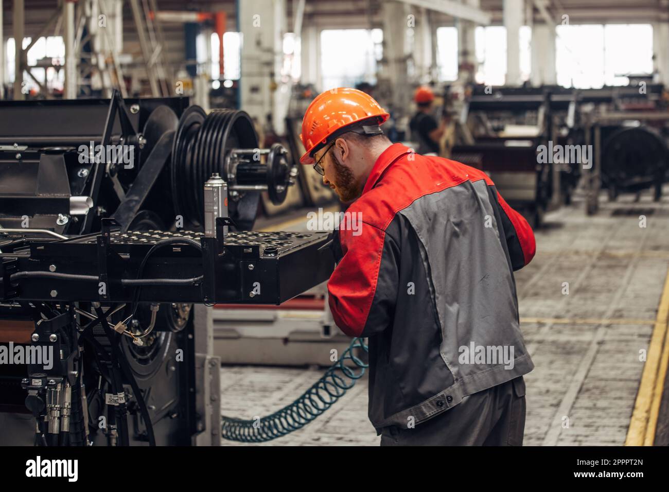 Industrial worker assembles agricultural machine in workshop. Stock Photo