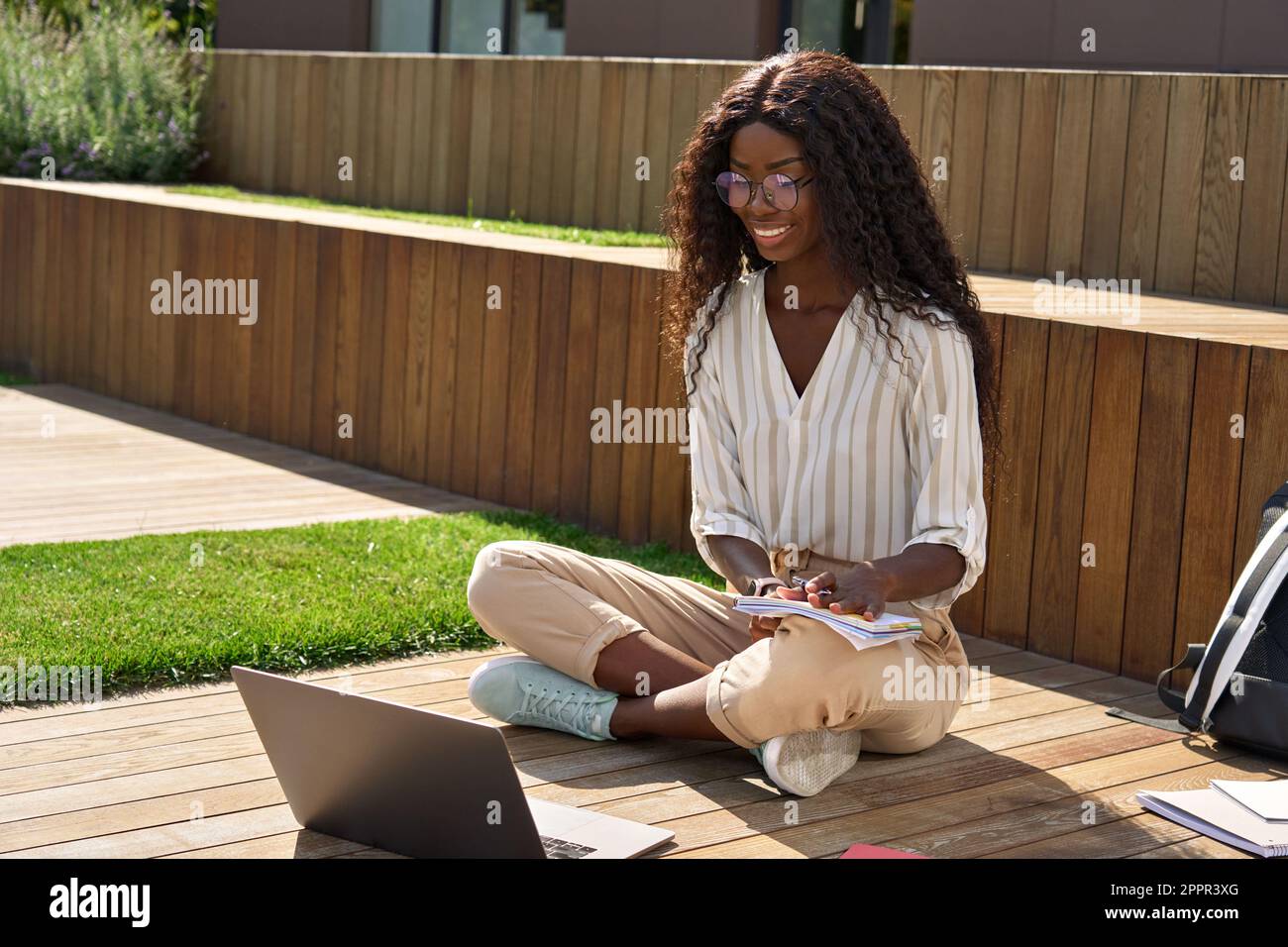 Happy African girl student studying online using laptop sitting outside ...