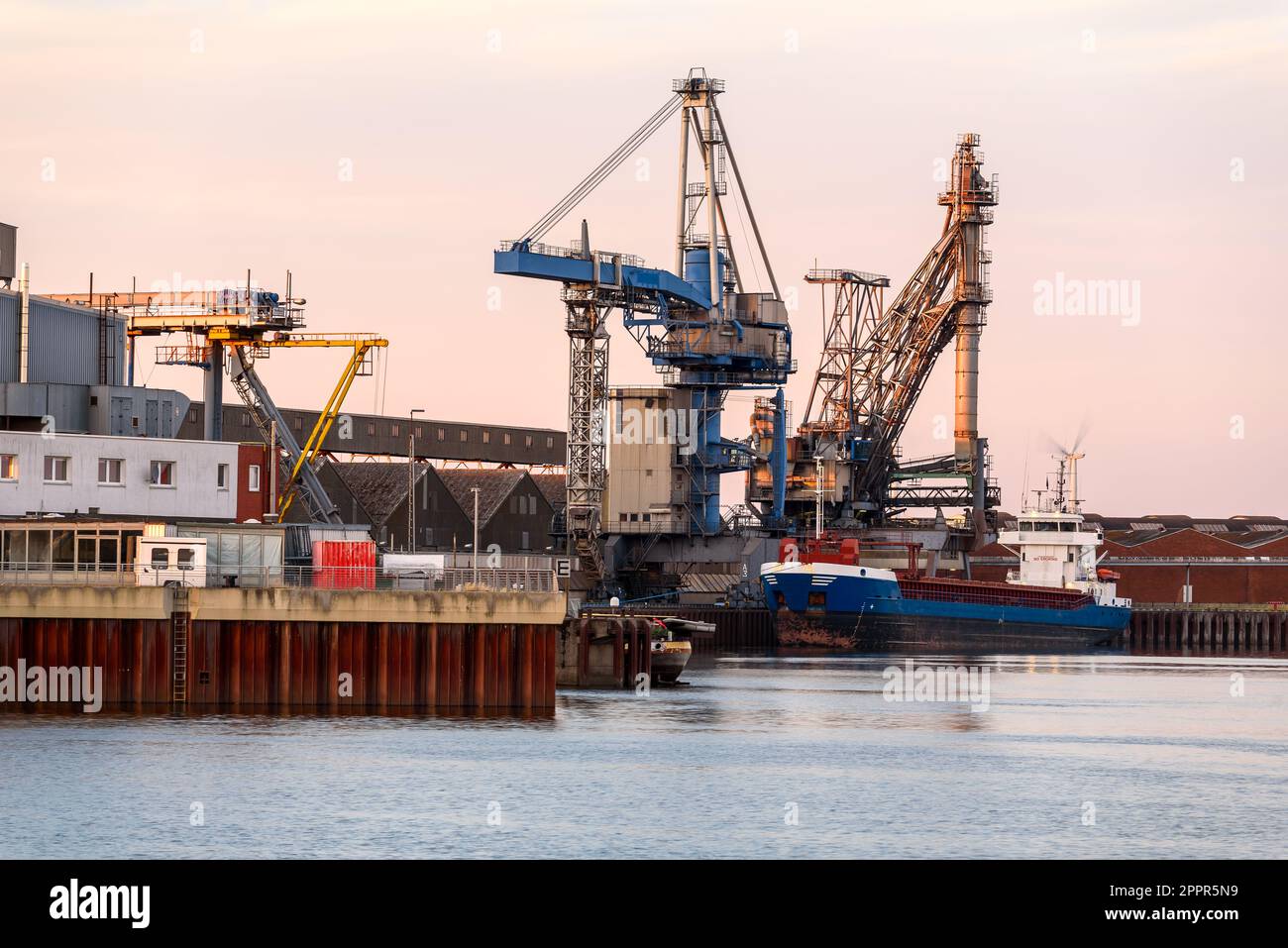 Cargo ship moored to a commercial dock at a river harbour at sunset Stock Photo