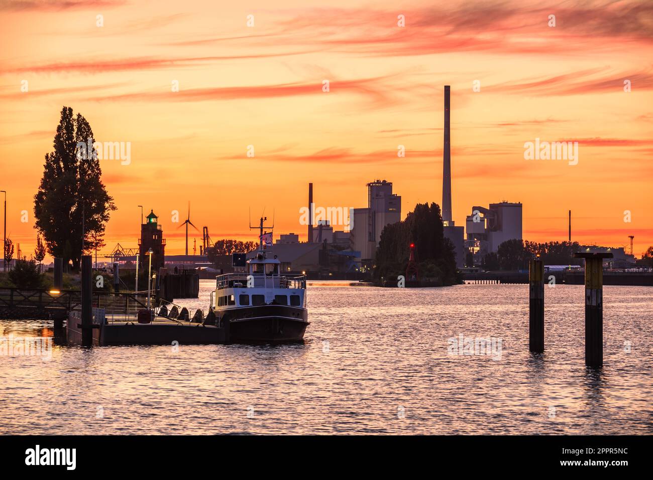 Orange sunset sky over a river harbour. Factories and wind turbines are in background. Stock Photo