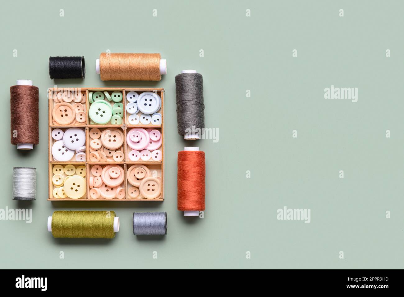 Composition with box of different buttons and thread spools on grey background Stock Photo