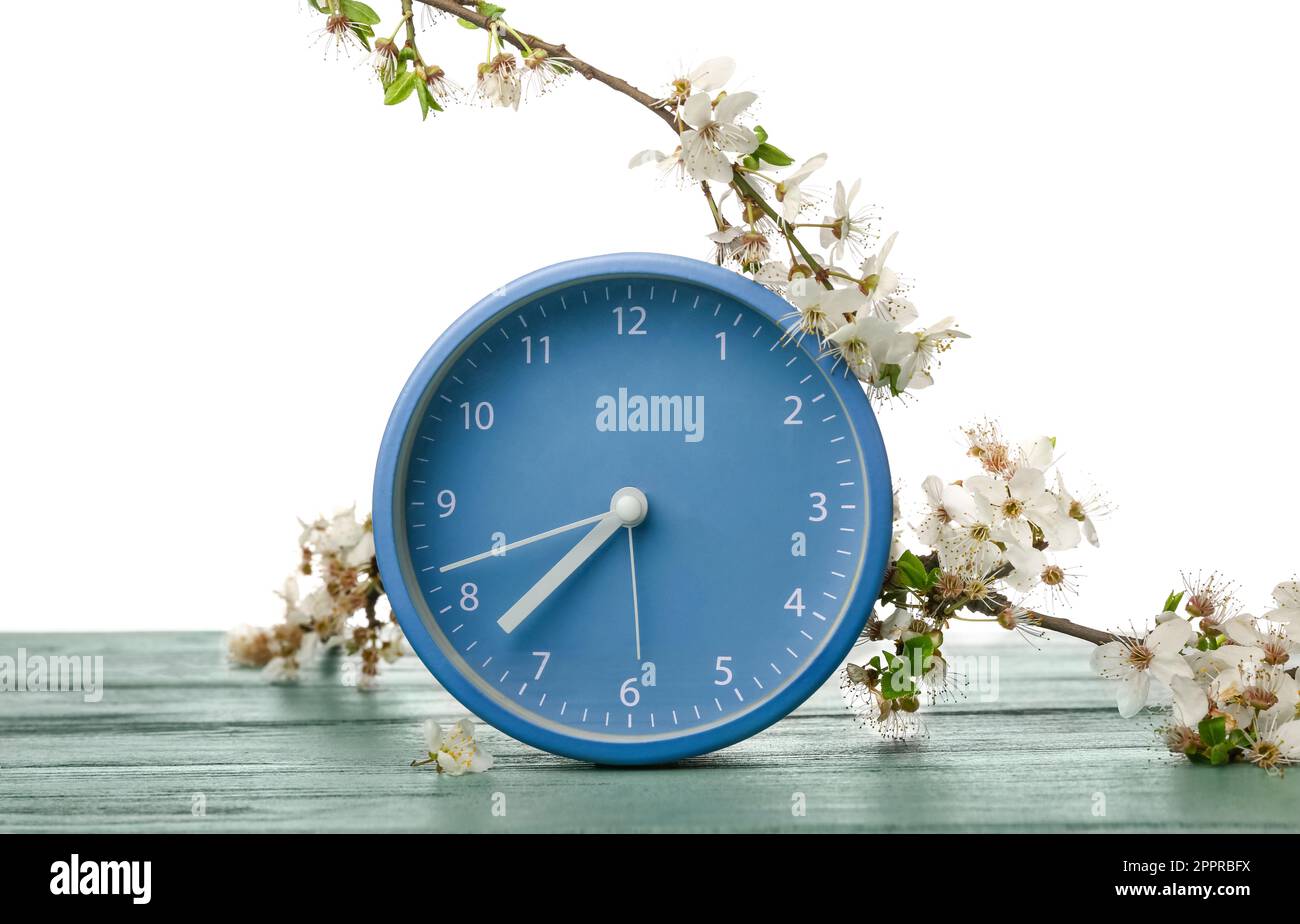 Blooming spring branches and clock on table against white background ...