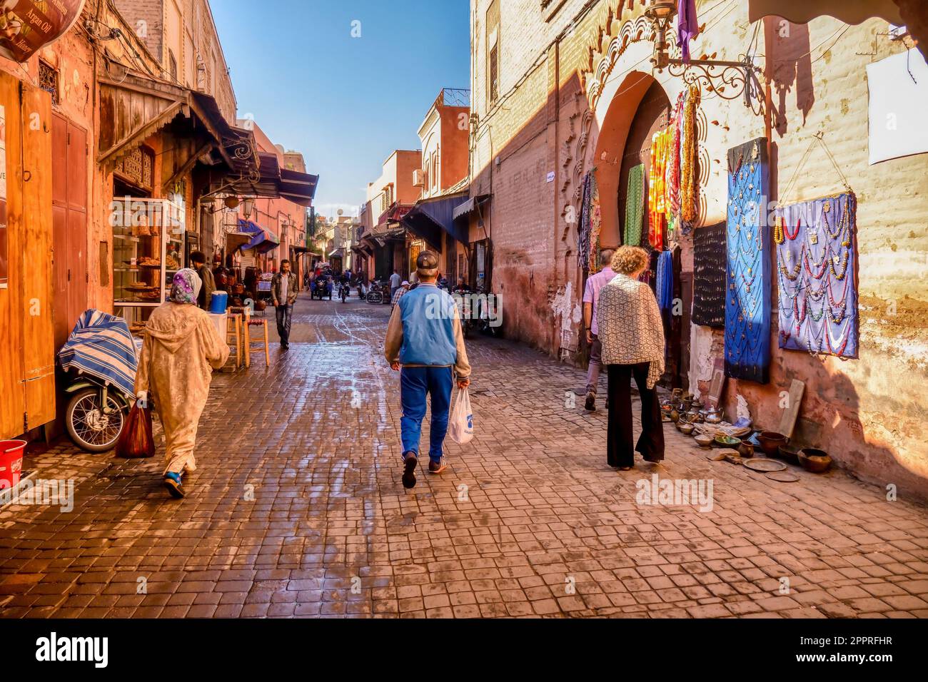 Marrakech, Morocco - October 19, 2015. Tourists and locals walking along a street in the Old City souk in early morning as shops open up for the day. Stock Photo