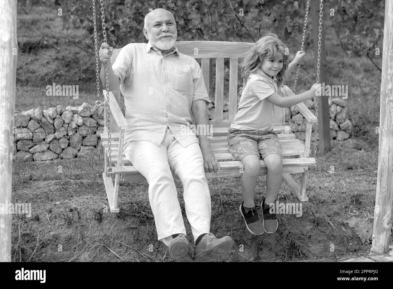Child boy and grandfather swinging in summer garden. Grand dad and