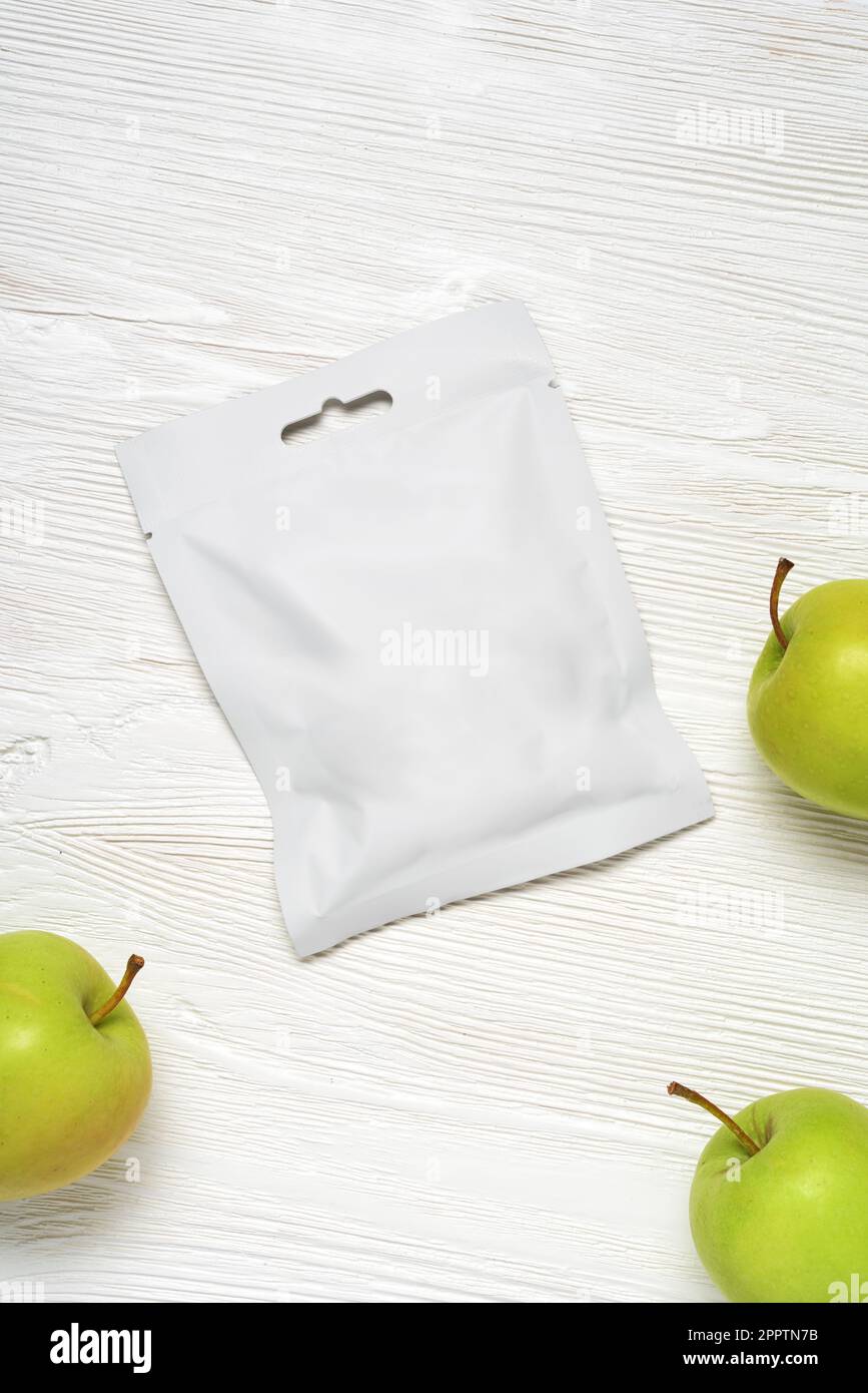 White plastic sachet packet with apples on wood table. Mockup template