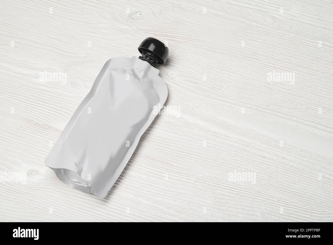 White empty plastic pouch for baby food, fruit puree on wood table. Mock-up template for design. Stock Photo