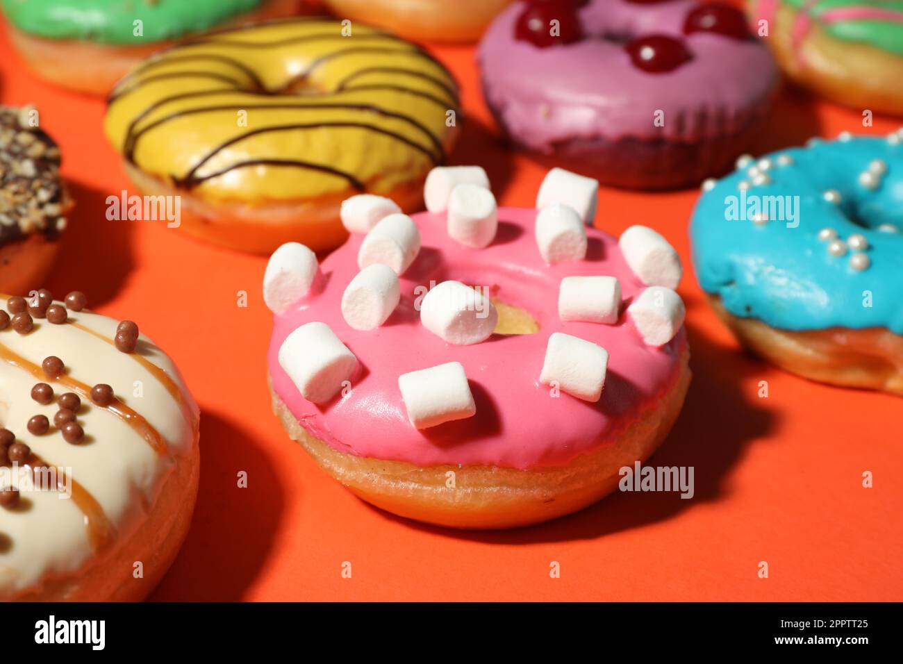 Sweet tasty glazed donuts on coral background, closeup Stock Photo