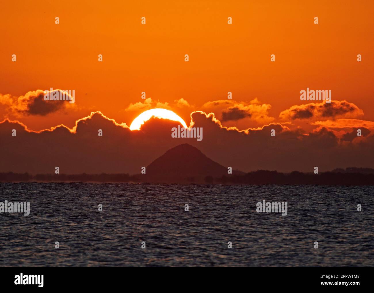 Portobello, Edinburgh, Scotland, UK. 25th April 2023. A nippy sunrise 2 degrees at dawn by the Firth of Forth with the sun slowly rising over the dark clouds on the horizon. Pictured: Berwick Law in the distance. Credit: Arch White/alamy live news. Stock Photo