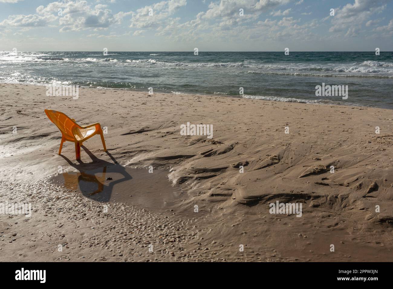 Plastic chair on sunny wet, sandy ocean beach, Bat Yam, Israel Stock Photo