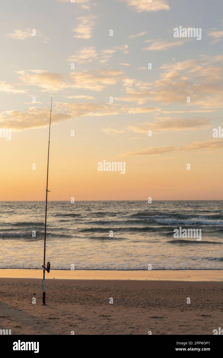 Fishing pole in sand on tranquil ocean beach at sunset, Bat Yam, Israel Stock Photo