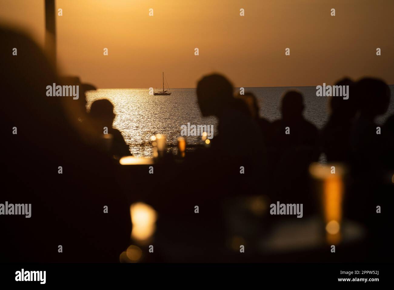 Silhouetted people drinking beer on ocean waterfront patio at sunset Stock Photo