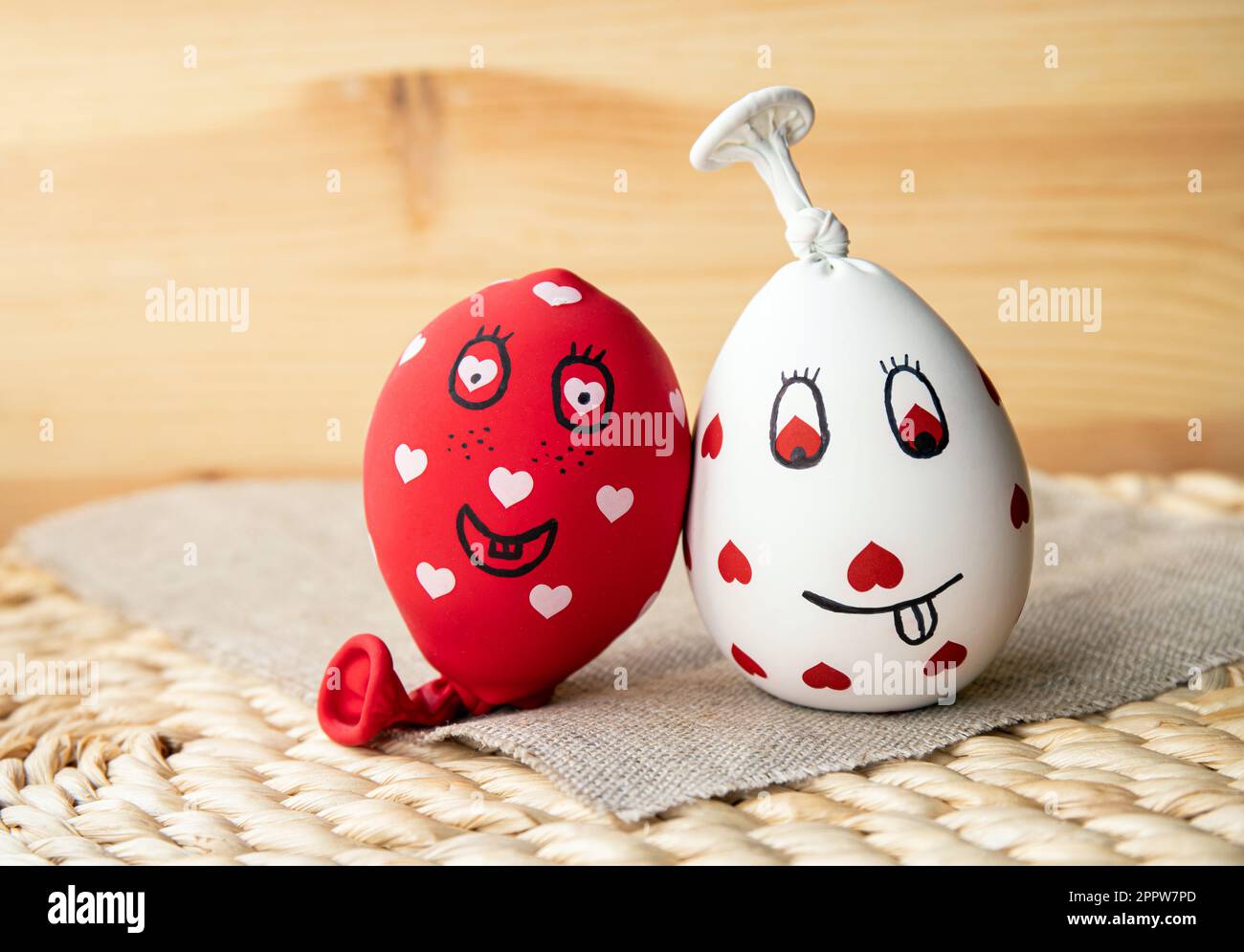 Two funny homemade sensory stress balls, made of balloons and filled with flour. Red and white balls with hearts and funny drawn faces. Stock Photo