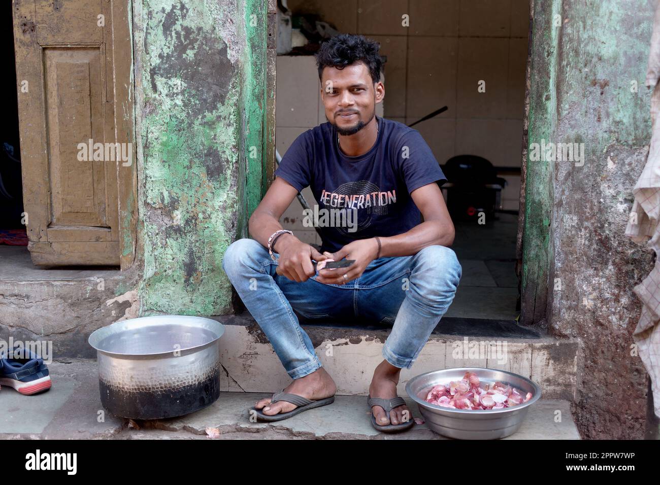 A young man in Darukhana slum area, Mazagaon, Mumbai, India, cutting onions to prepare a meal Stock Photo