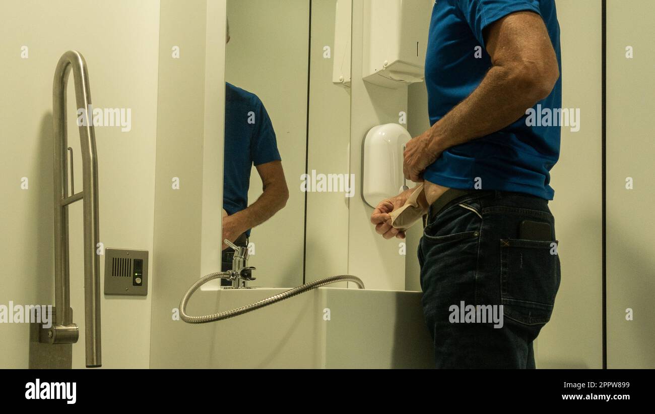 Mature man with stoma emptying ileostomy bag/pouch in airport terminal toilet designed exclusively for people with ileostomy or colostomy. Stock Photo