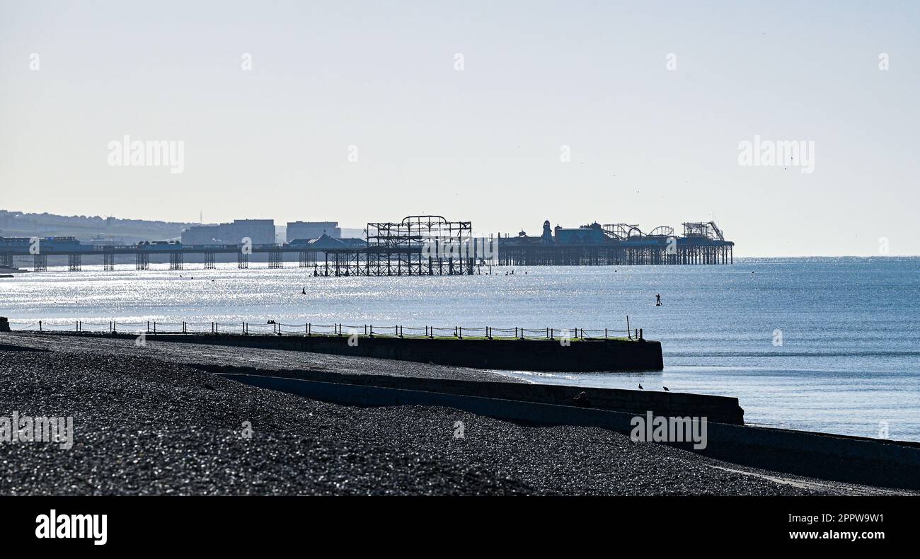 Brighton UK 25th April 2023 - A paddle boarder out at sea off Hove beach with Brighton's two  piers in the background on a sunny but chilly morning along the South Coast : Credit Simon Dack / Alamy Live News Stock Photo