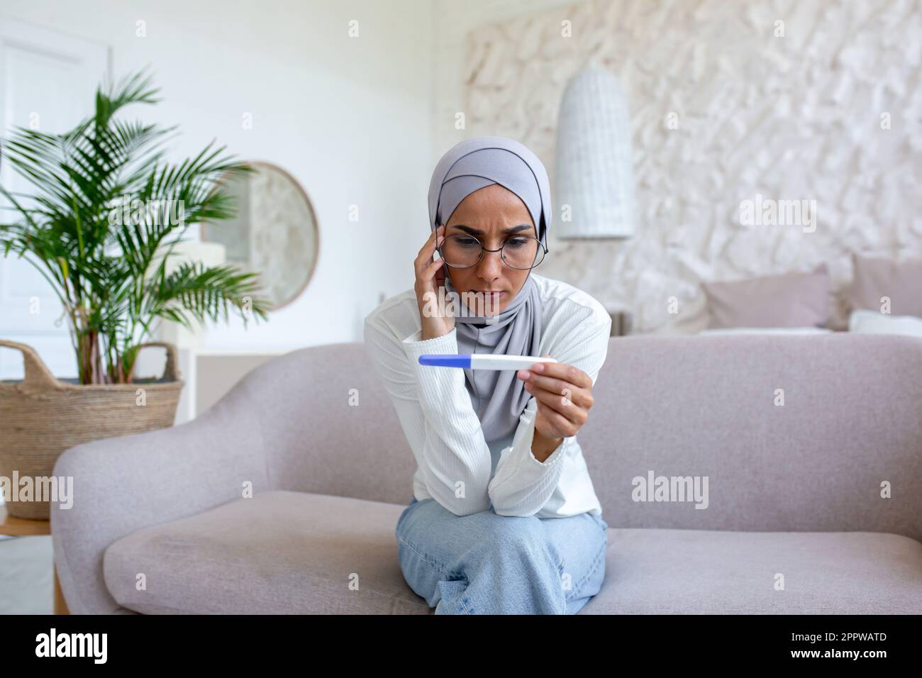 Upset and depressed woman sitting on sofa at home, muslim woman got bad ...
