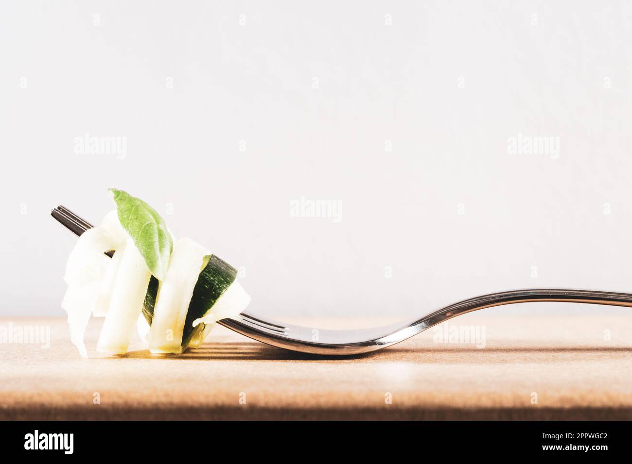 Zucchini zu Spagetti geschnitten und freigestellt mit viel licht gedreht auf einer Gabel und mit einem Basilikumblatt garniert Stock Photo