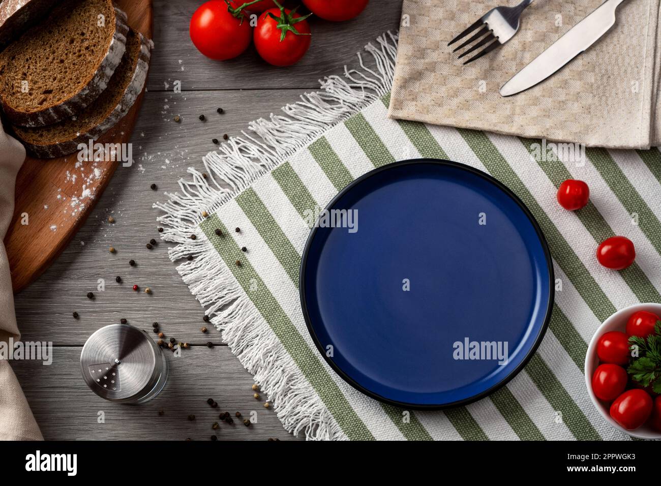 An empty blue plate as serving on the table. Table setting with vegetables and bread on a grey background. Stock Photo
