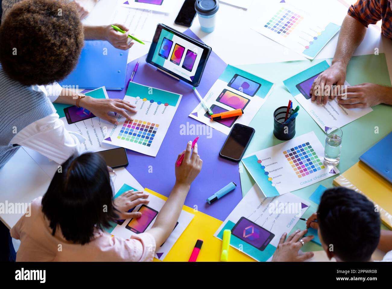 High angle of busy diverse designers using tablet and discussing visuals at design meeting Stock