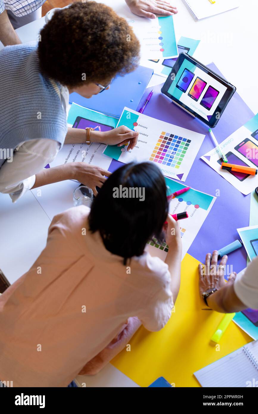 High angle of busy diverse designers using tablet and discussing visuals at design meeting Stock