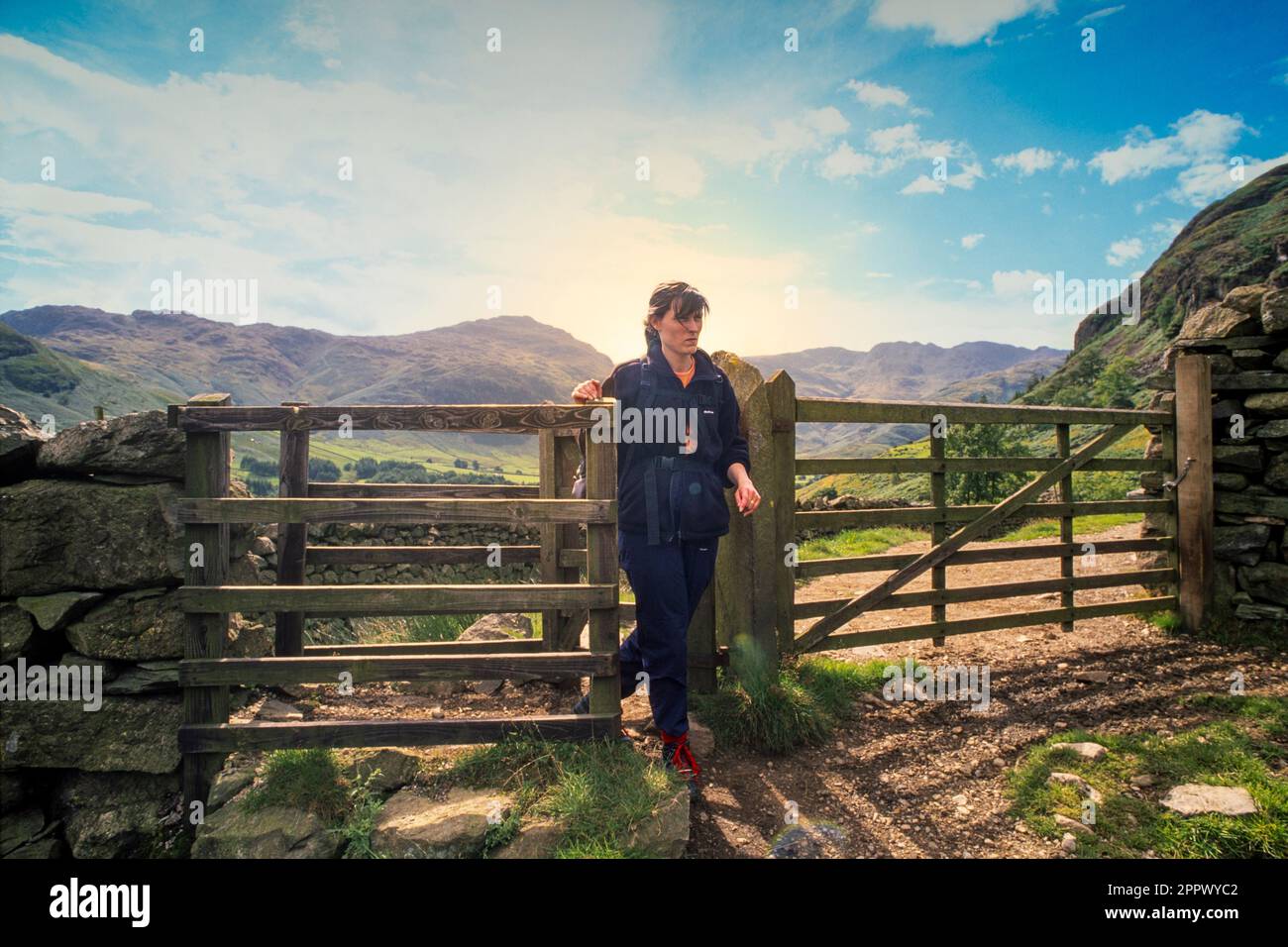 Archive photo of a young caucasian female walking through a wooden kissing gate in the Cumbrian countryside. UK Stock Photo