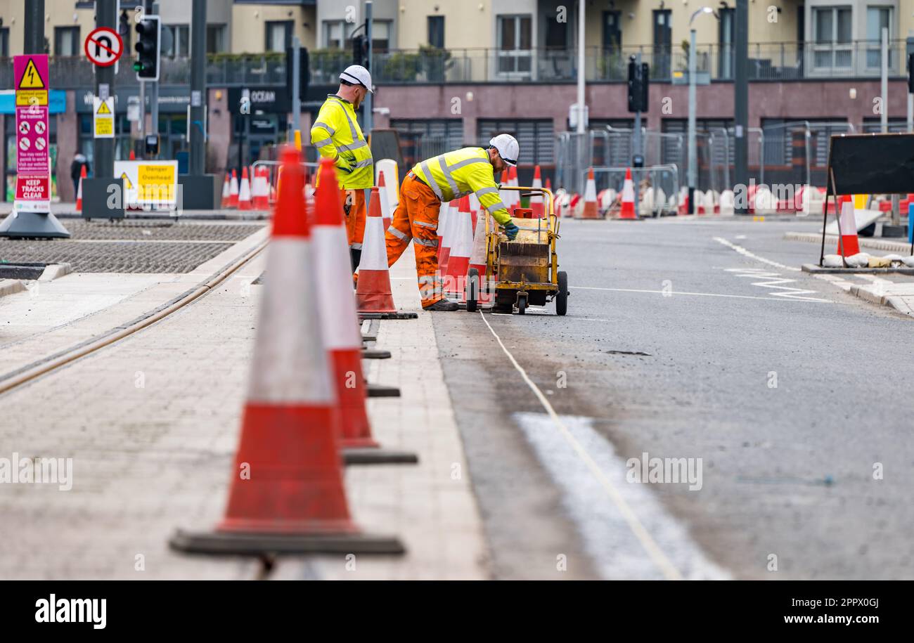Two workmen painting white lines on roadside next to tram tracks, Leith, Edinburgh, Scotland, UK Stock Photo